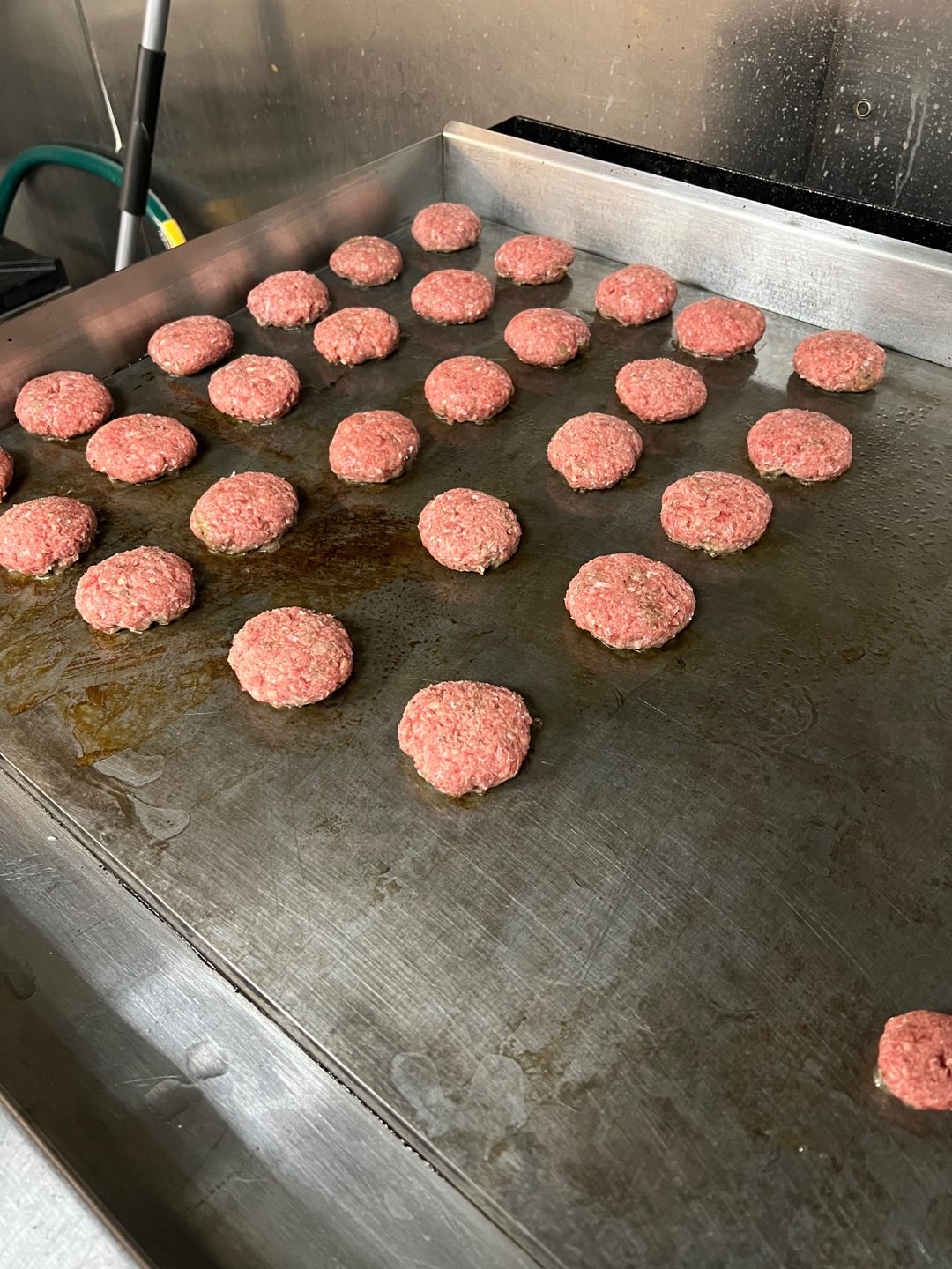 Fresh hand-pressed beef patties lined up on the food truck's flat-top griddle