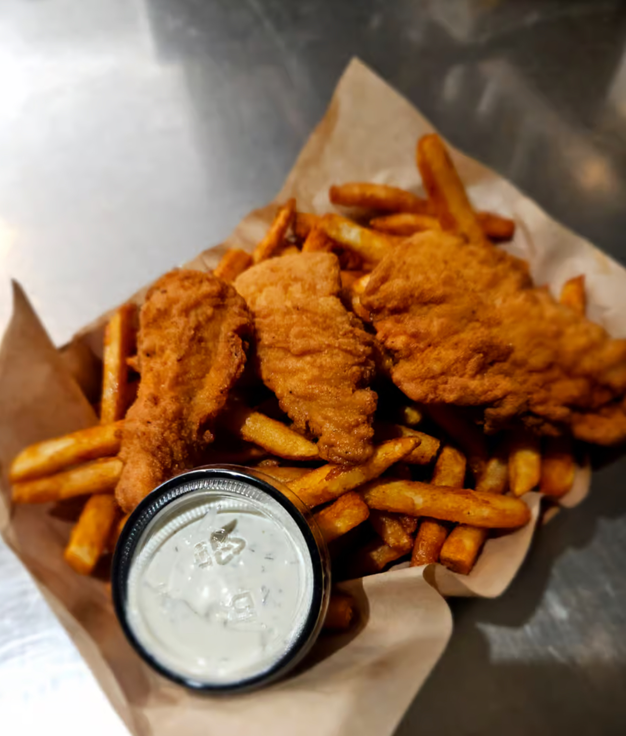 Basket of crispy fried chicken tenders and seasoned fries with a cup of ranch