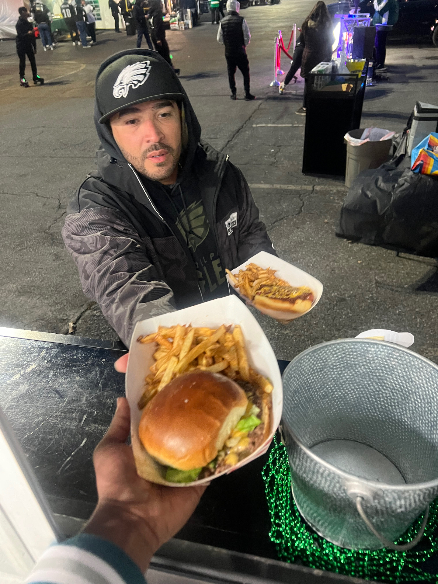 Server handing a smashburger and hand-cut fries to a customer at a night-time tailgate catering event