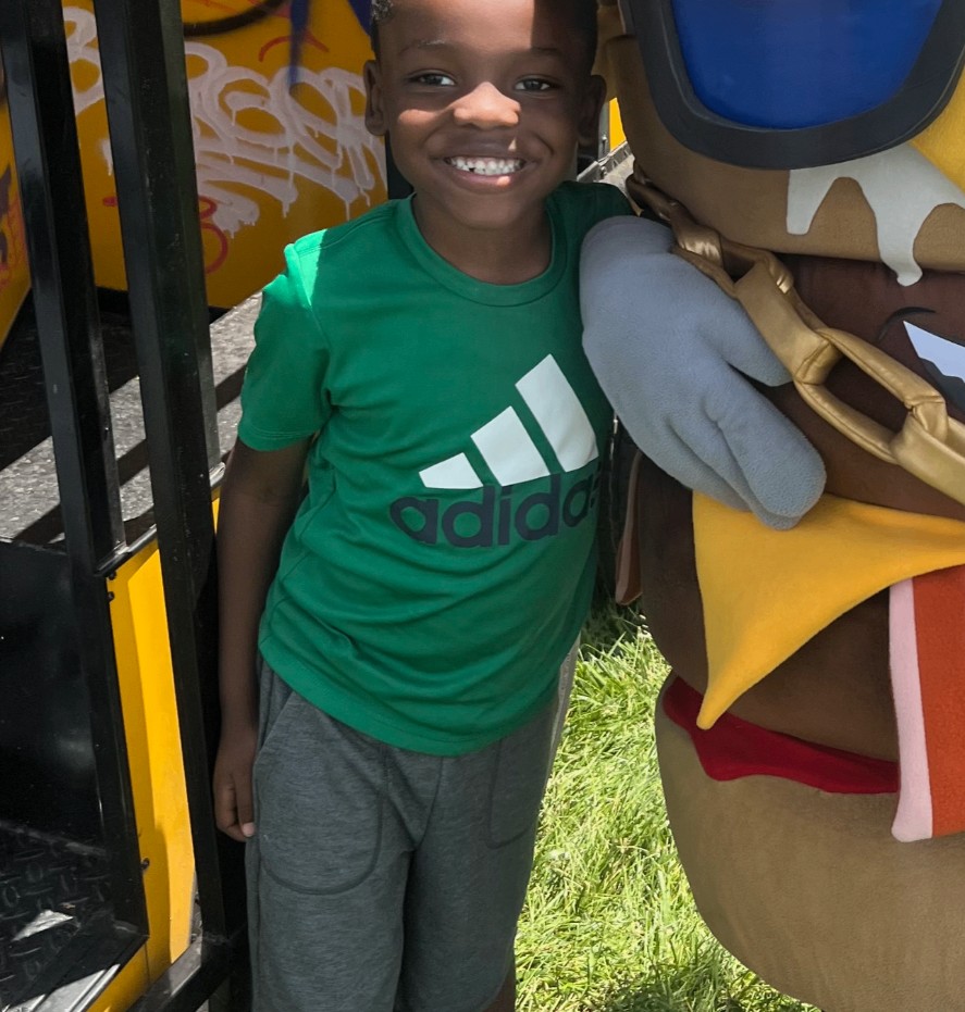 Young fan posing with the Mallie's Burgers mascot beside the food truck at a family event