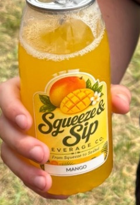 Close-up of the Squeeze & Sip mango lemonade label on a can held by a guest at an outdoor Mallie's Burgers event